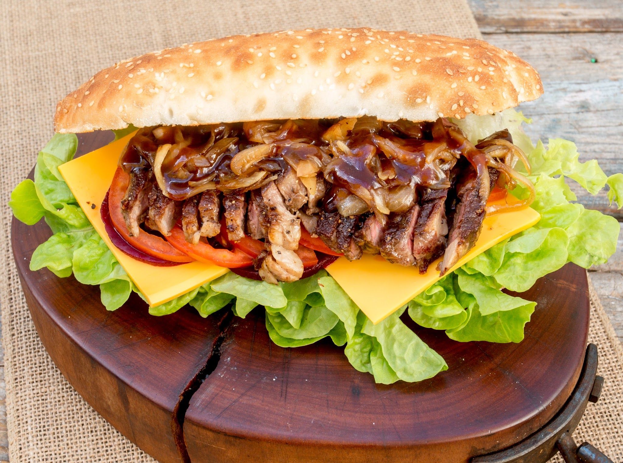 Steak sandwich with caramelised onions, cheddar and salad on a sesame roll