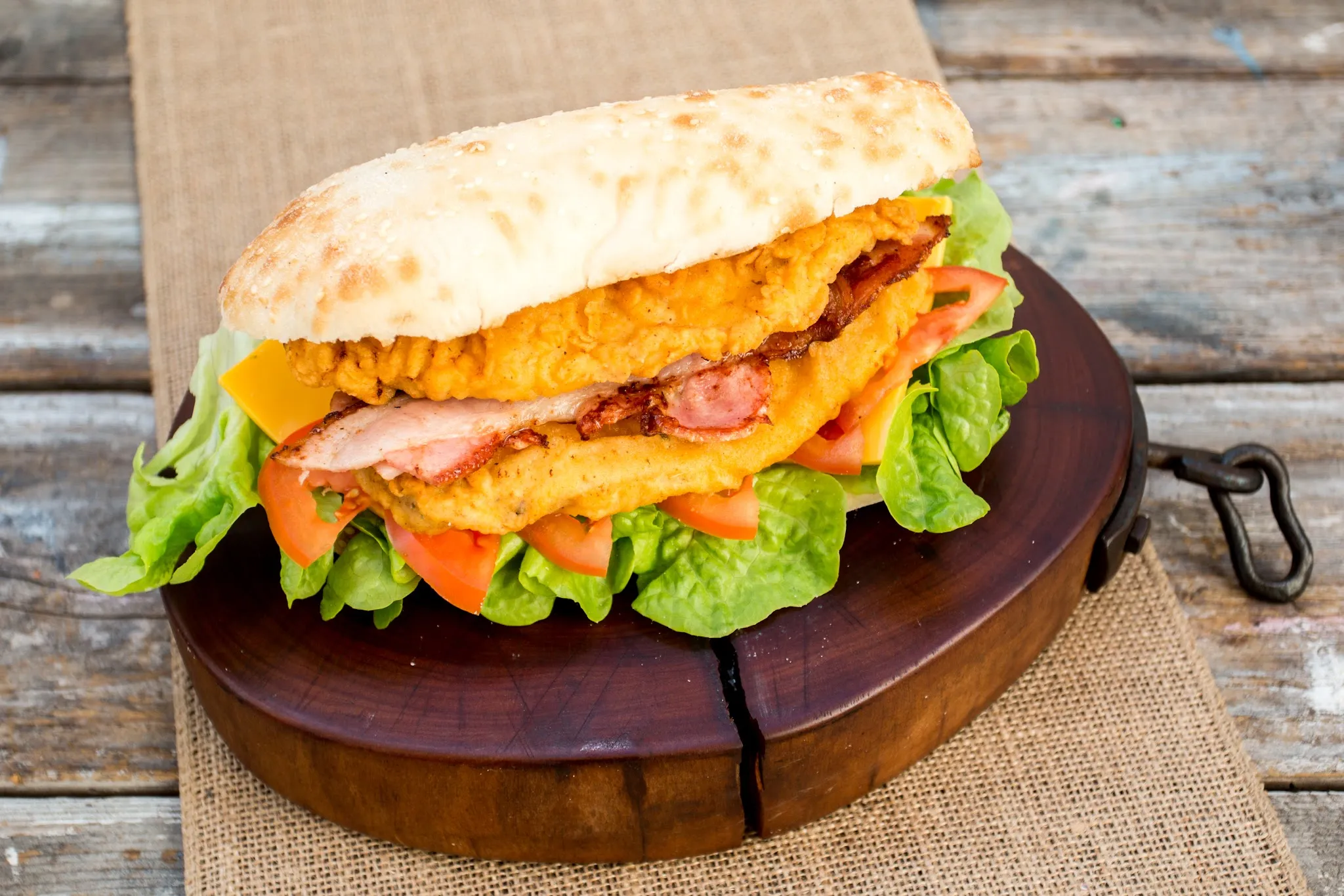 Crispy chicken and bacon burger with cheese, tomato and lettuce on a sesame roll