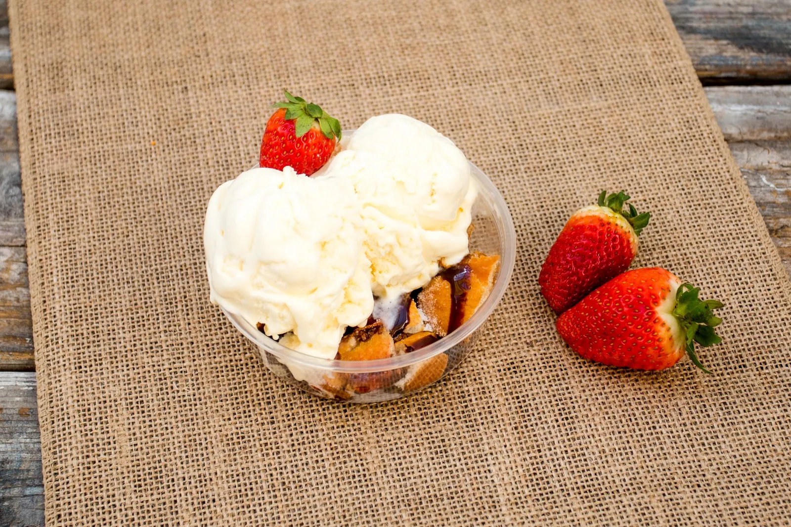 Vanilla ice cream scoops with fresh strawberries in a takeaway tub