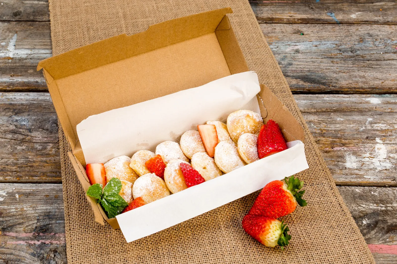 Sugar-dusted mini Dutch pancakes with strawberries in a takeaway box